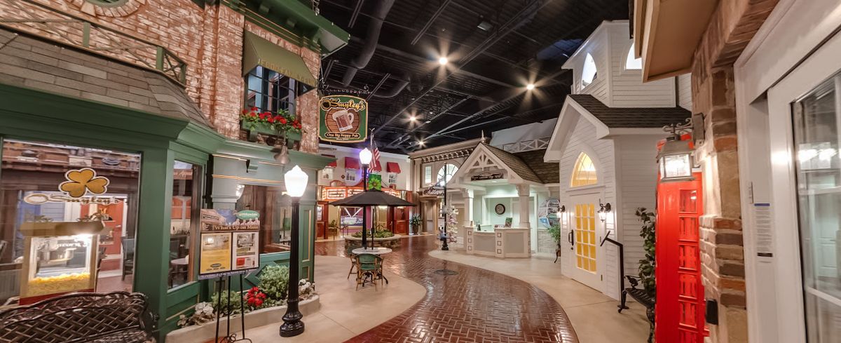 An indoor village setting with charming shops and cobblestone walkways, illuminated by street lamps.
