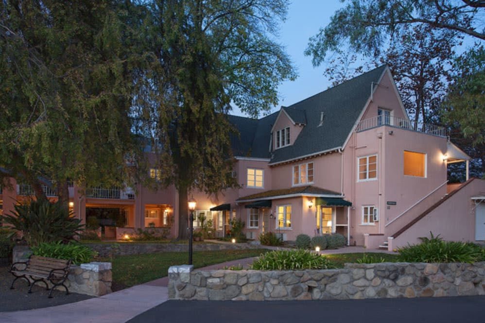 A charming house exterior lit up in the evening, surrounded by trees.