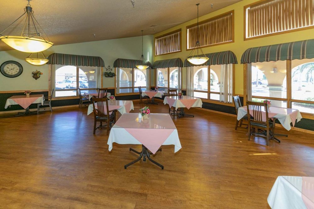 An empty dining area with several tables and chairs, covered with tablecloths, in a well-lit restaurant interior.