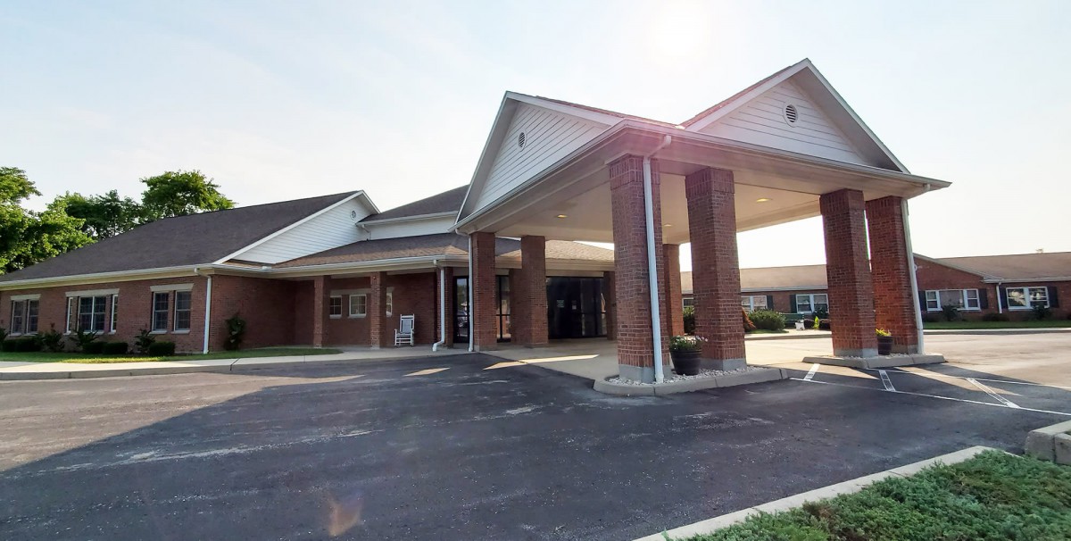 A brick building with a covered entrance and driveway, illuminated by sunlight.
