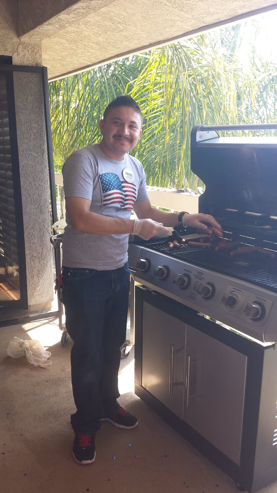 A person smiling while grilling on a patio during the day.