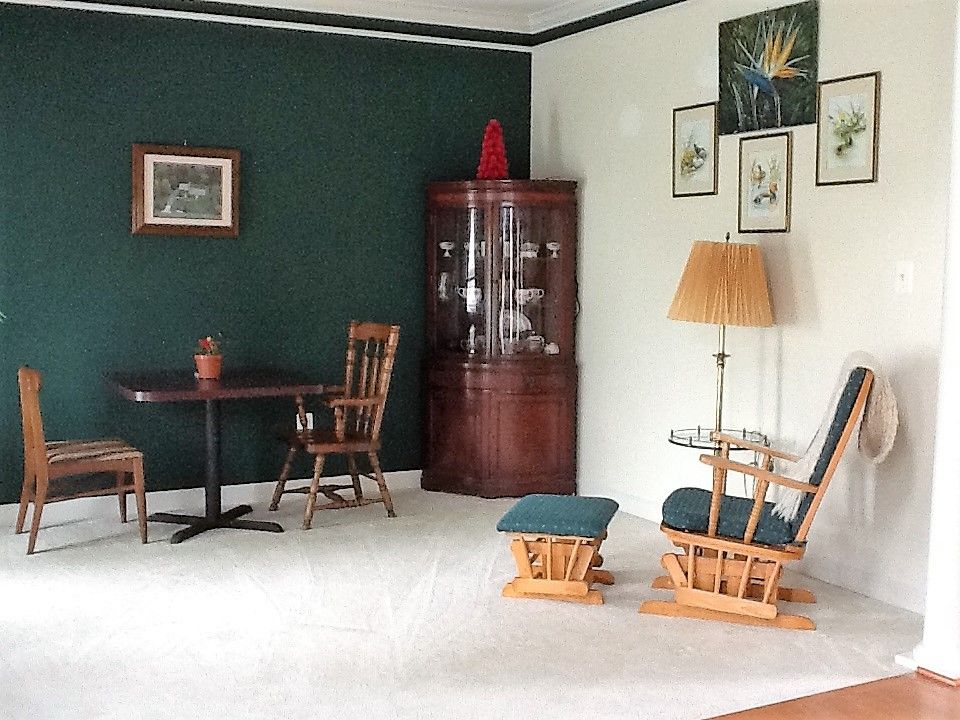 A cozy living room with wooden furniture, a table and chairs, a glass cabinet, a floor lamp, and decorative wall art.