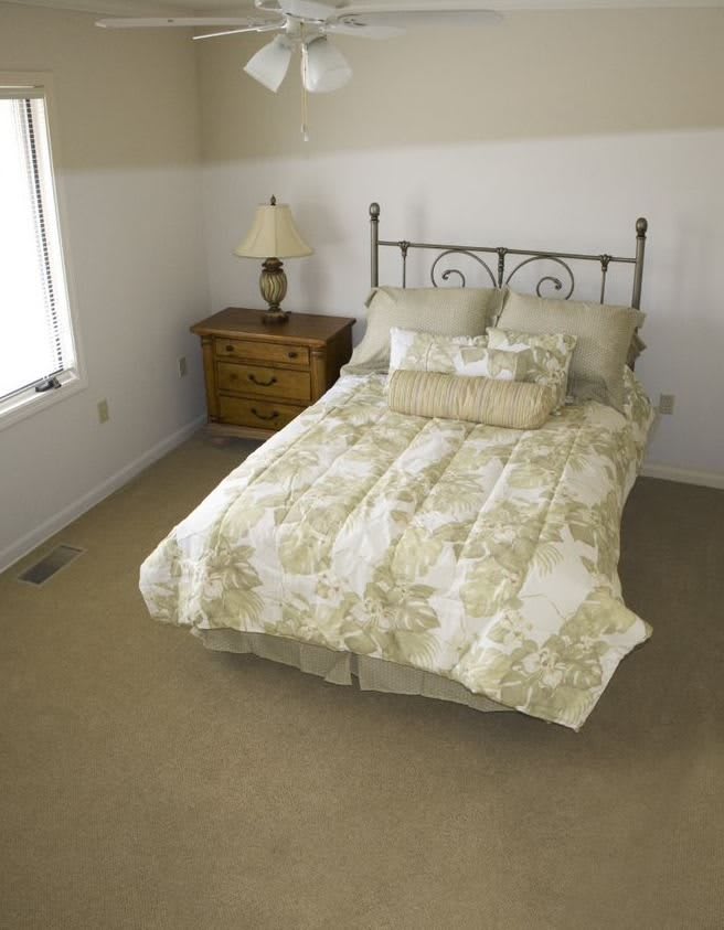 A cozy bedroom with a neatly made bed, nightstand, and lamp.