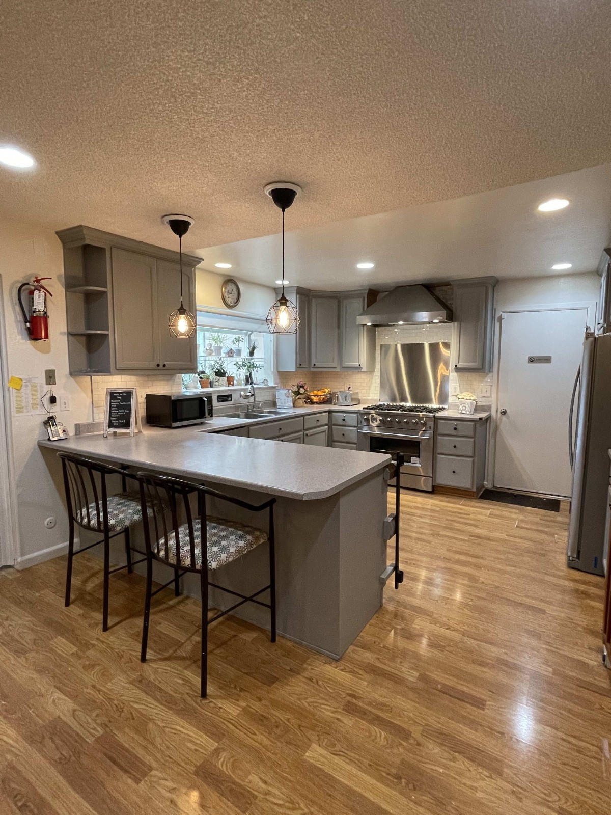 A modern kitchen with gray cabinets, an island with seating, and stainless steel appliances.