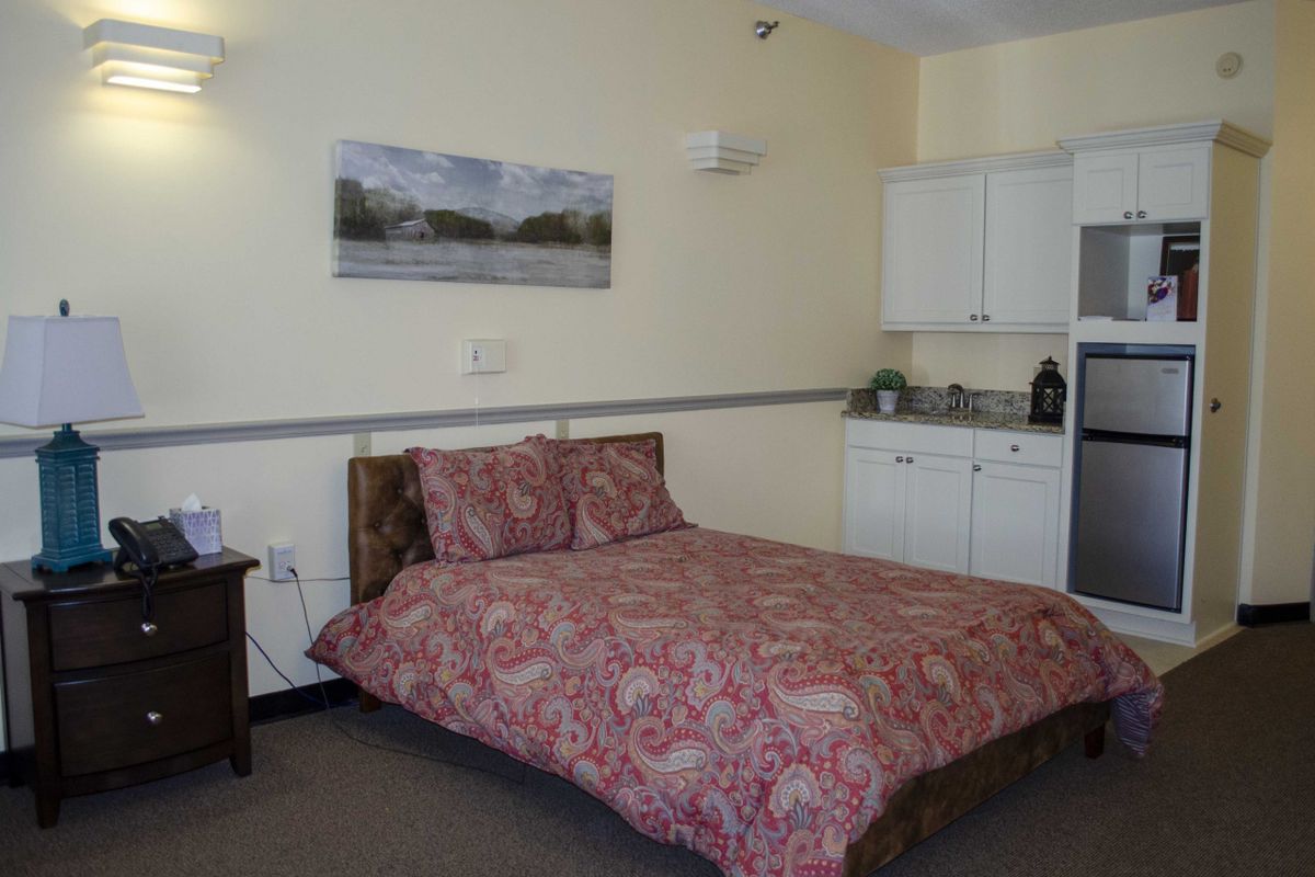 A cozy bedroom with a kitchenette featuring a patterned bedspread and wall art.