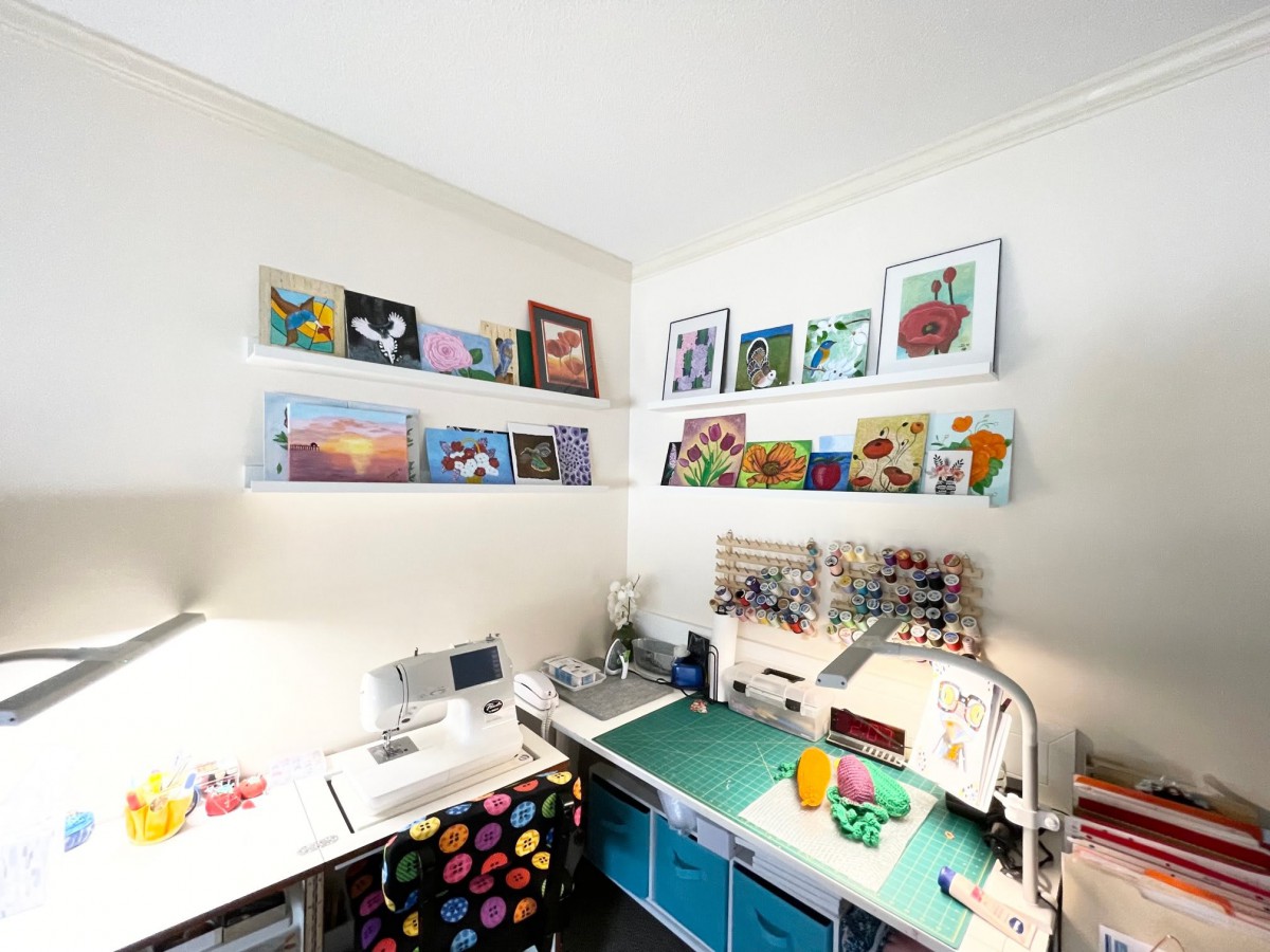 A well-organized craft room featuring colorful paintings on shelves, a sewing machine, and various art supplies.