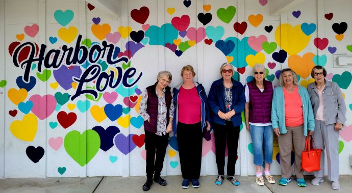 A group of people standing in front of a colorful heart-themed mural.