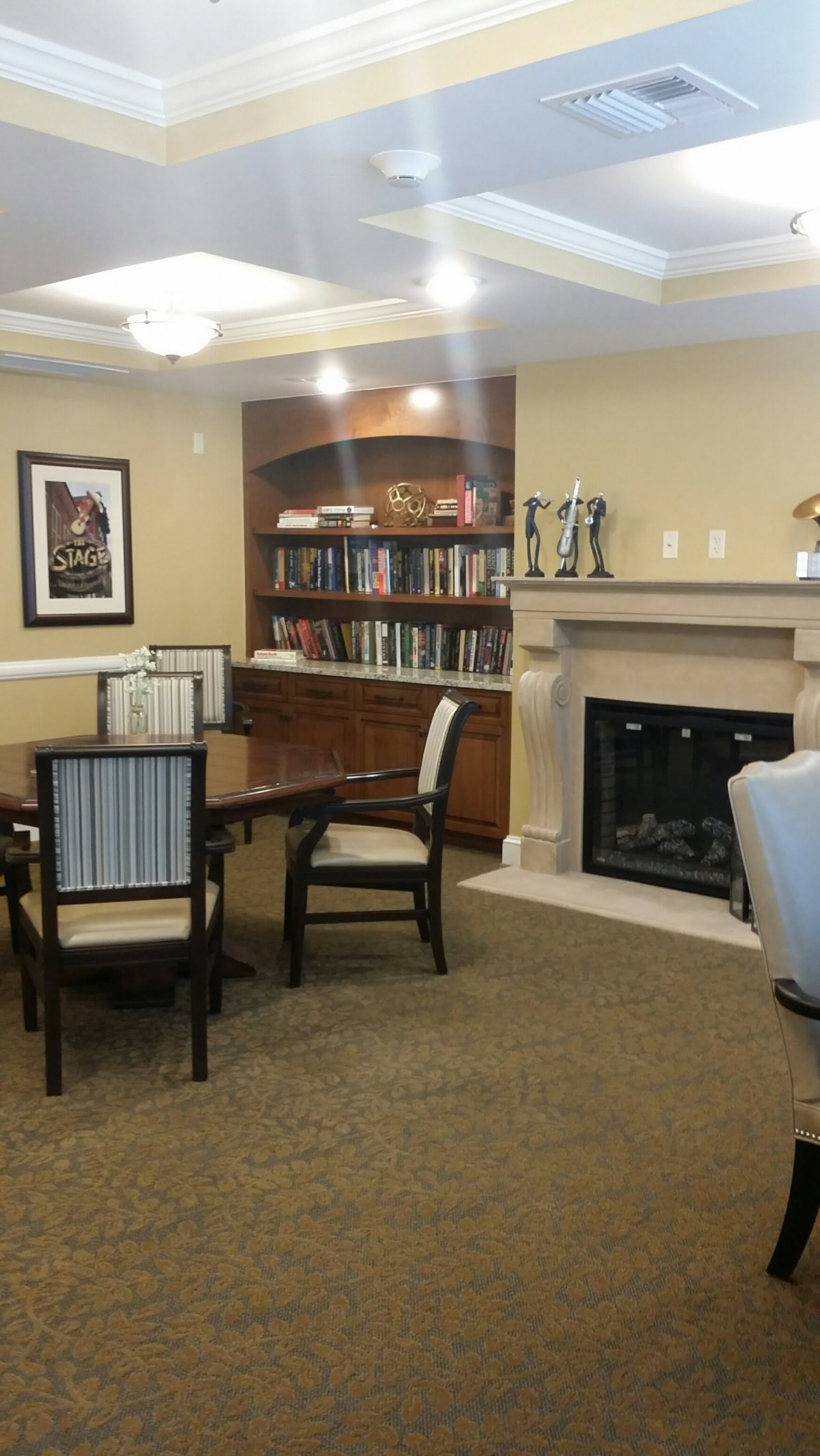 A cozy reading room with a fireplace and bookshelves, featuring a table and chairs.