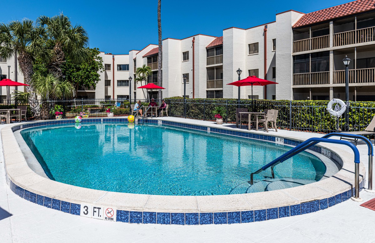 An inviting swimming pool at a residential apartment complex, surrounded by lounge chairs and red umbrellas.