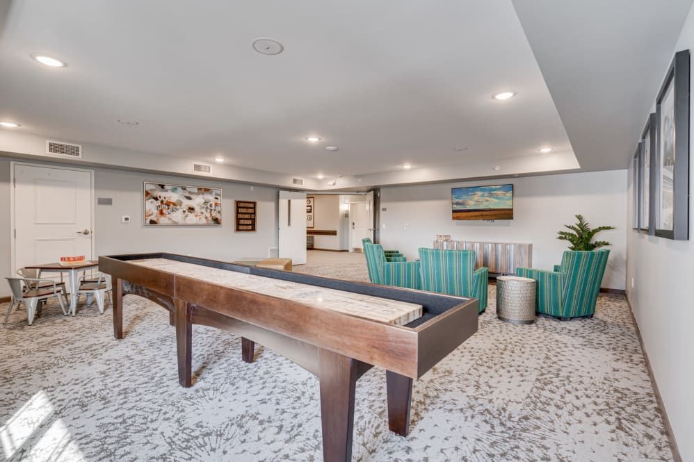 A modern game room featuring a shuffleboard table and comfortable seating.