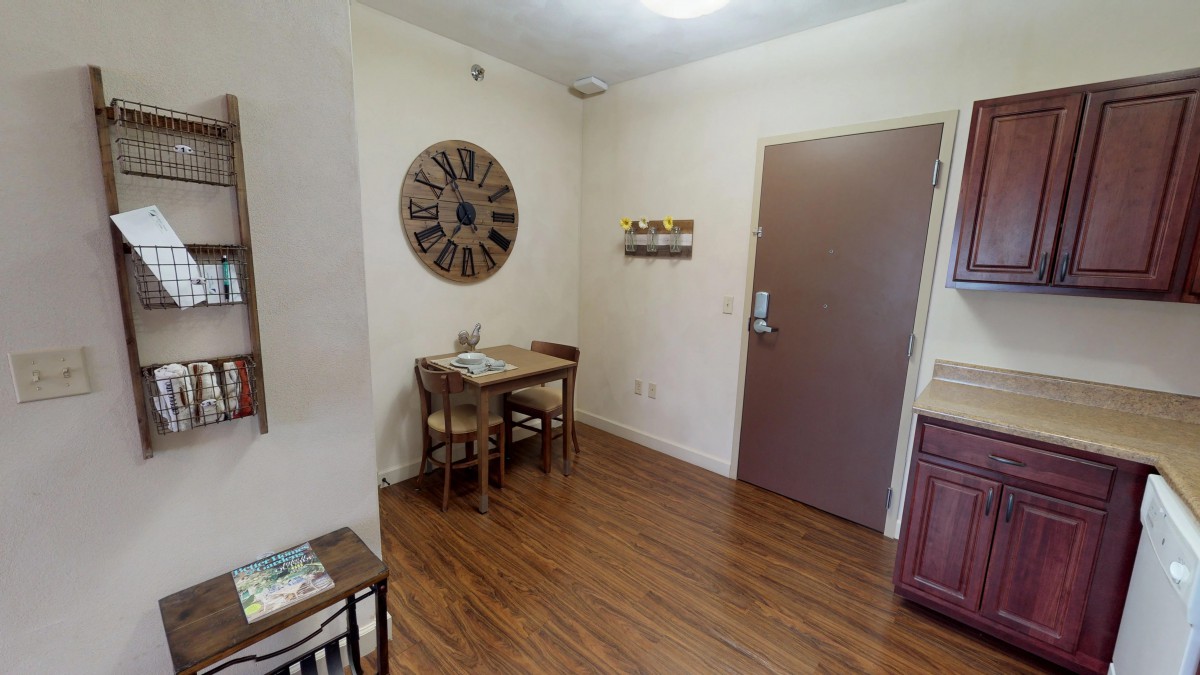 A cozy room with a wooden table and chairs, a large wall clock, and a decorative door.
