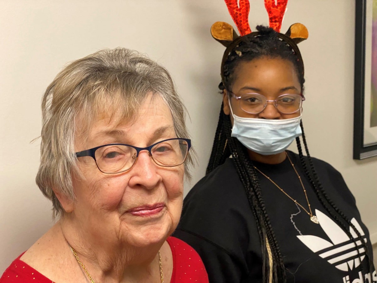 An elderly woman and a young woman with reindeer antlers and a mask sitting together.