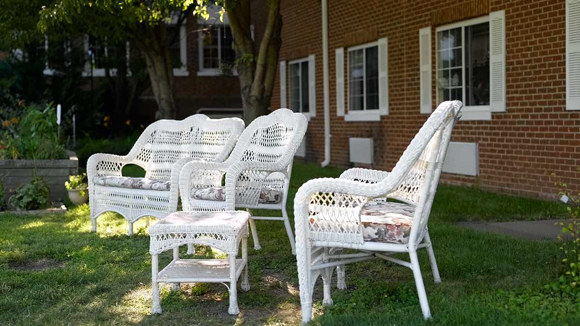 Wicker chairs and a table set on a lawn outside a brick building.