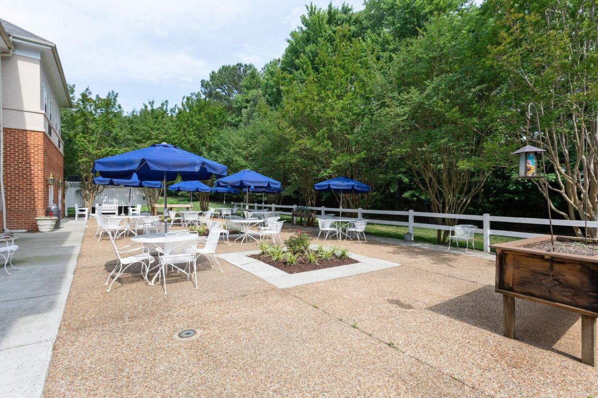An outdoor patio with tables and blue umbrellas surrounded by lush greenery.