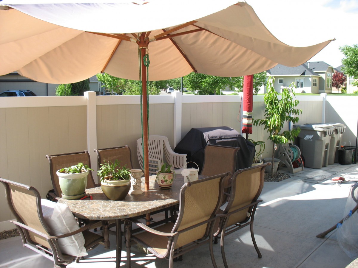 A cozy patio setup with a large umbrella over a table and chairs, surrounded by potted plants.