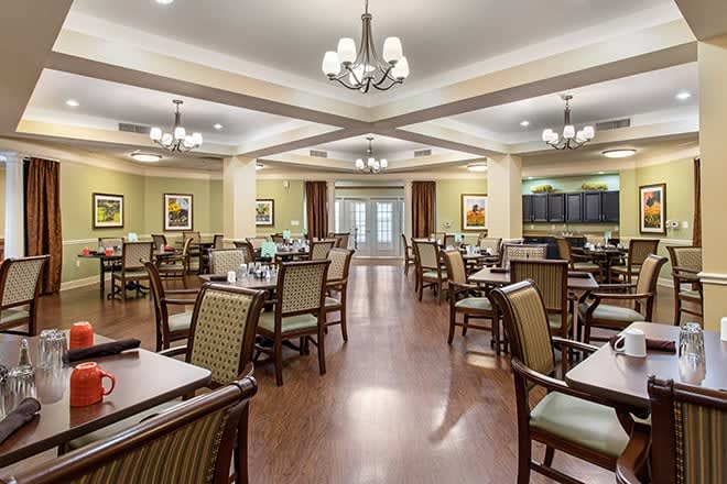 A spacious and elegantly decorated dining room with multiple tables and chairs, featuring chandeliers and wooden flooring.