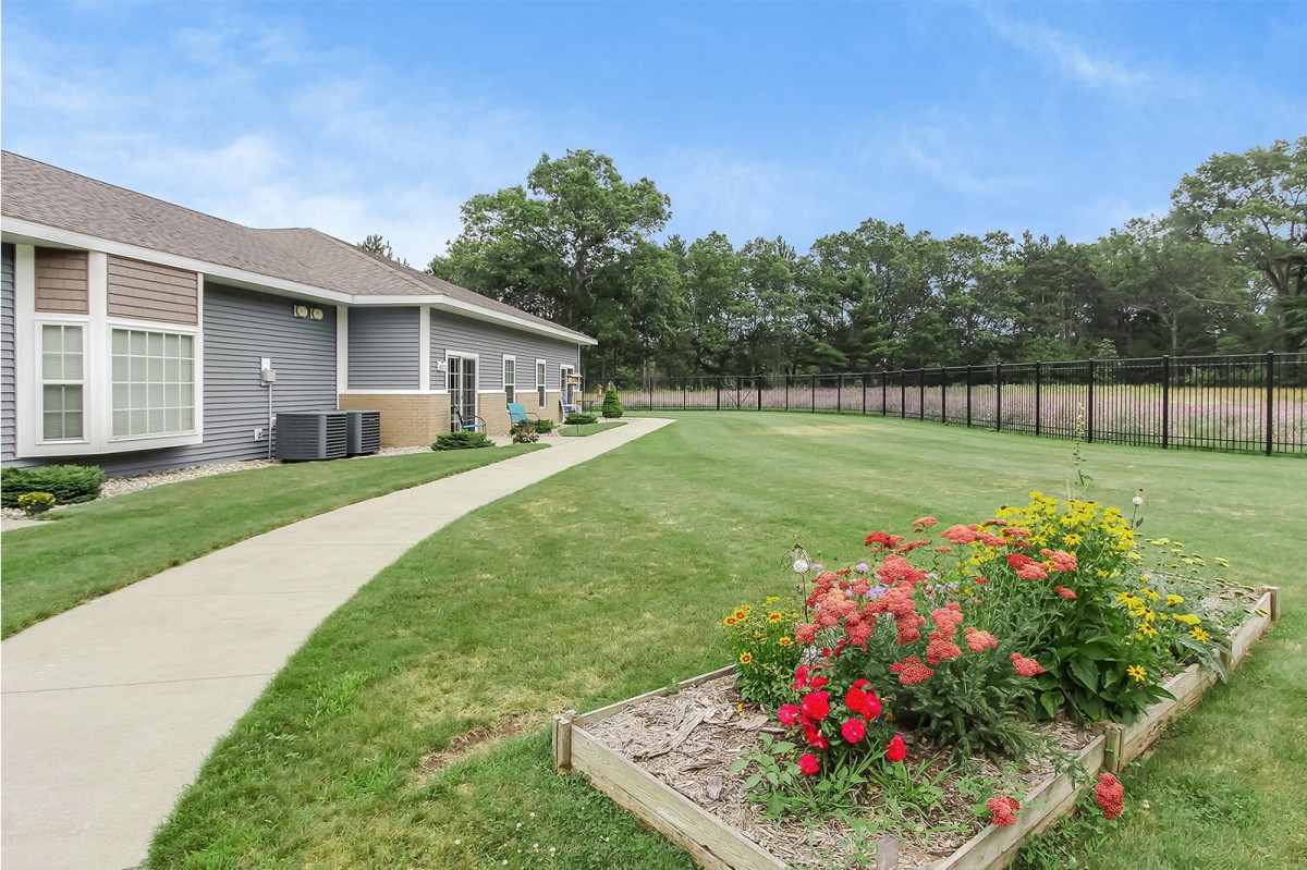 A well-maintained garden with vibrant flowers next to a building, featuring a clean pathway and a fence in the background.