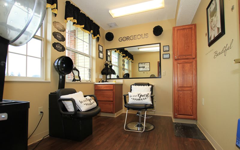 A stylish hair salon interior featuring a comfortable chair, large mirror, and wooden flooring.