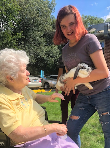 A joyful moment captured in the sun, as a young woman happily presents a rabbit to an elderly lady.