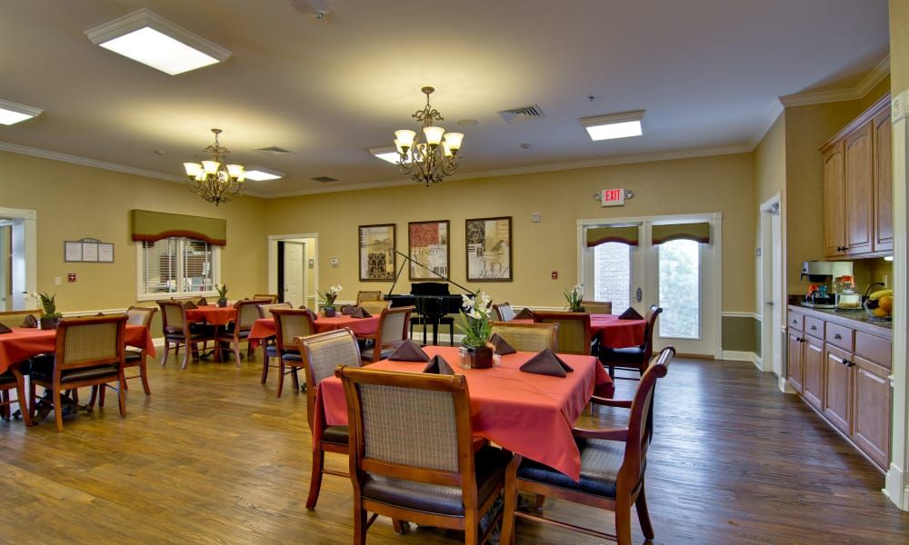 A cozy dining room setup with tables covered in red tablecloths and elegant chandeliers overhead.