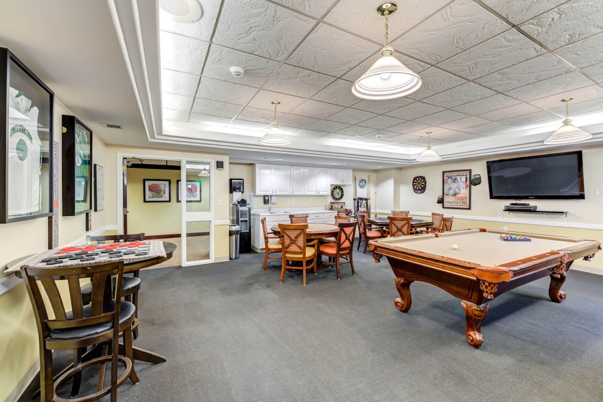 A spacious game room featuring a pool table, ample seating, and indoor lighting, decorated with various wall hangings.
