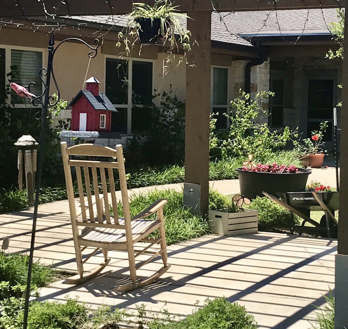 A peaceful garden patio with a wooden rocking chair basking in sunlight.