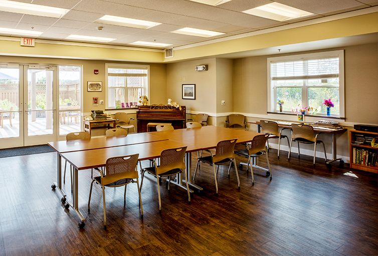 A spacious classroom with tables and chairs, featuring large windows allowing natural light in.