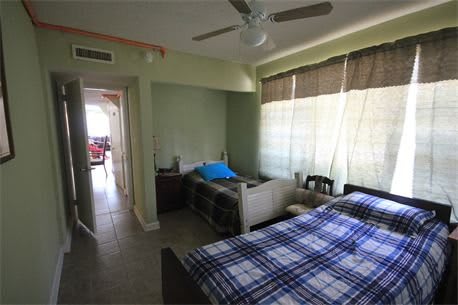 A cozy bedroom with a plaid-covered bed, ceiling fan, and large window with curtains.