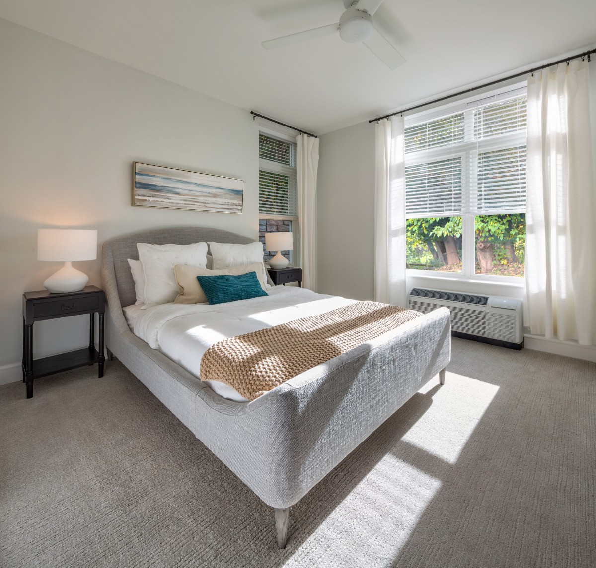 A bright and modern bedroom with minimalist decor, featuring a bed by large windows letting in natural light.