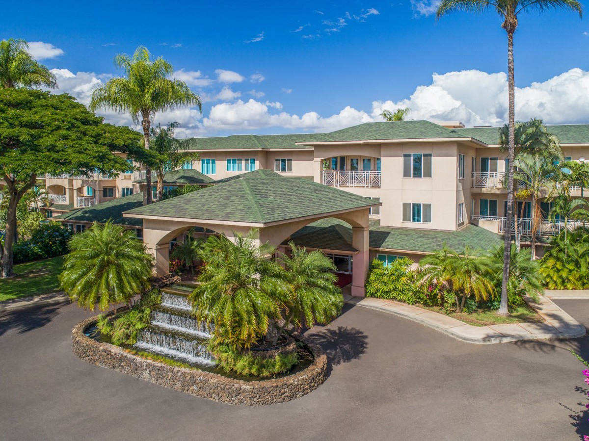 A tropical residential building with a fountain at the entrance surrounded by lush palm trees.