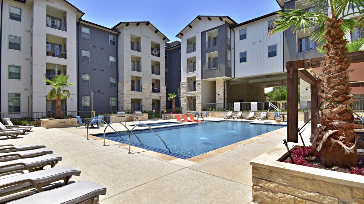 A modern apartment complex with a central swimming pool on a sunny day.