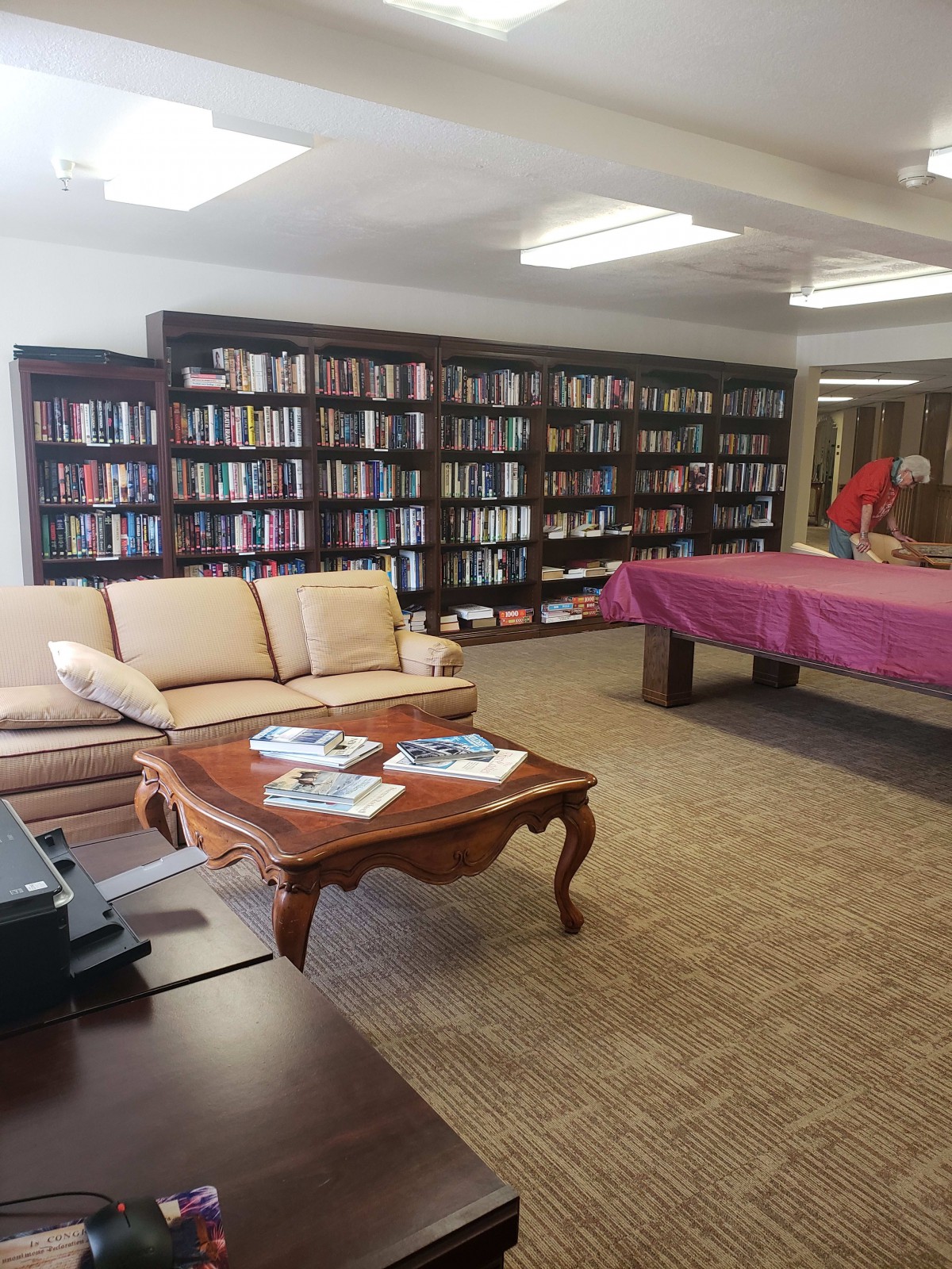A cozy library lounge with bookshelves, a sofa, and a pool table.