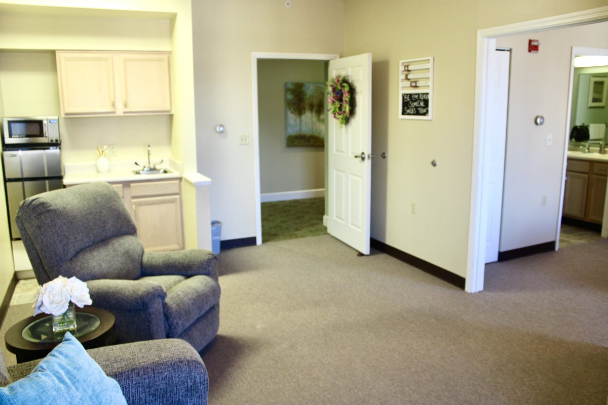 A cozy living room with a recliner and a kitchenette, featuring an open door adorned with a wreath.