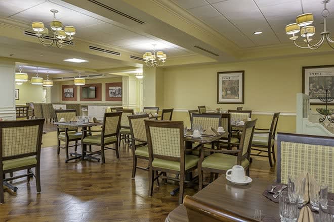 An empty dining room with neatly arranged tables and chairs, featuring cozy lighting and wooden flooring.