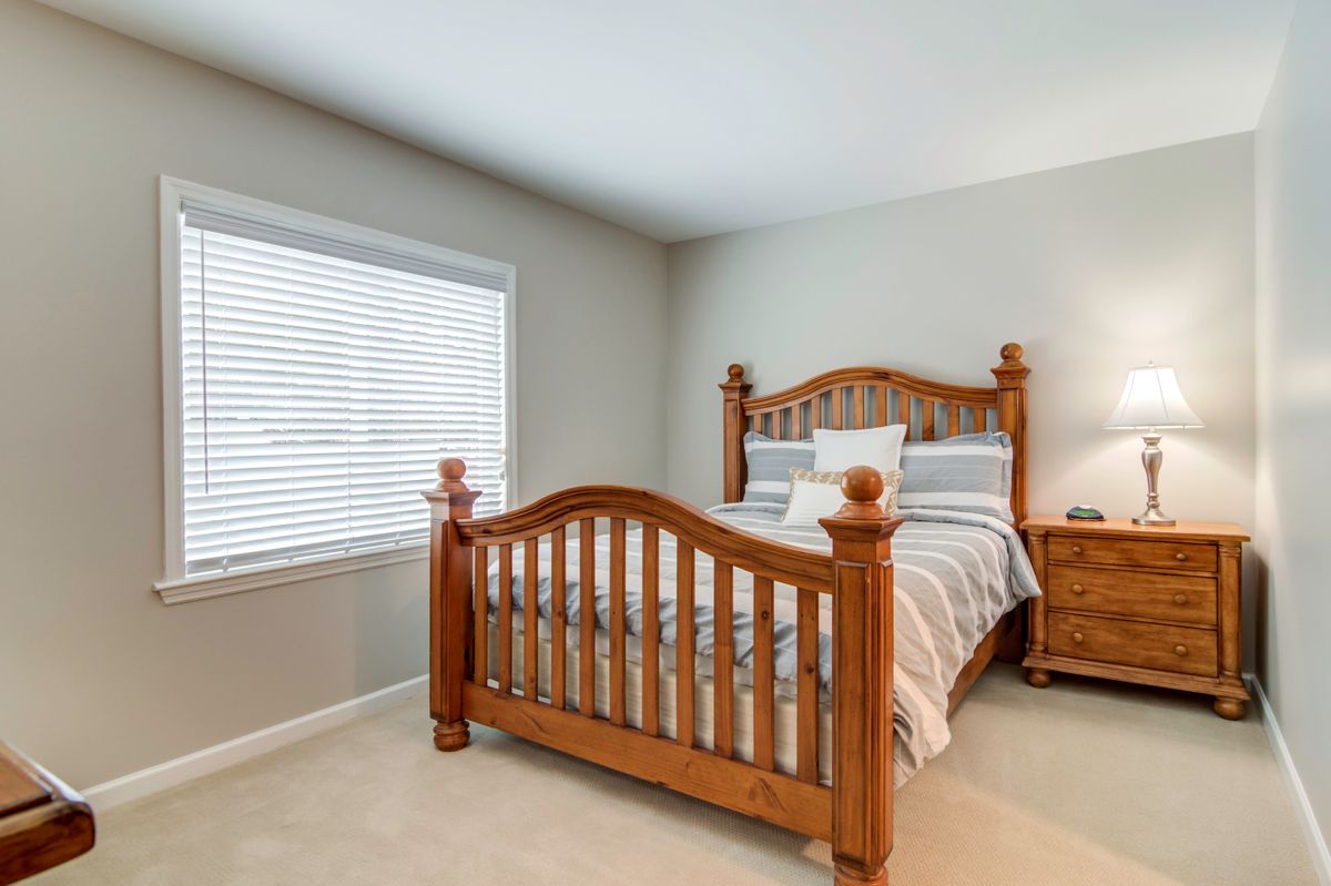 A cozy bedroom with a wooden bed frame and striped bedding next to a window with blinds.