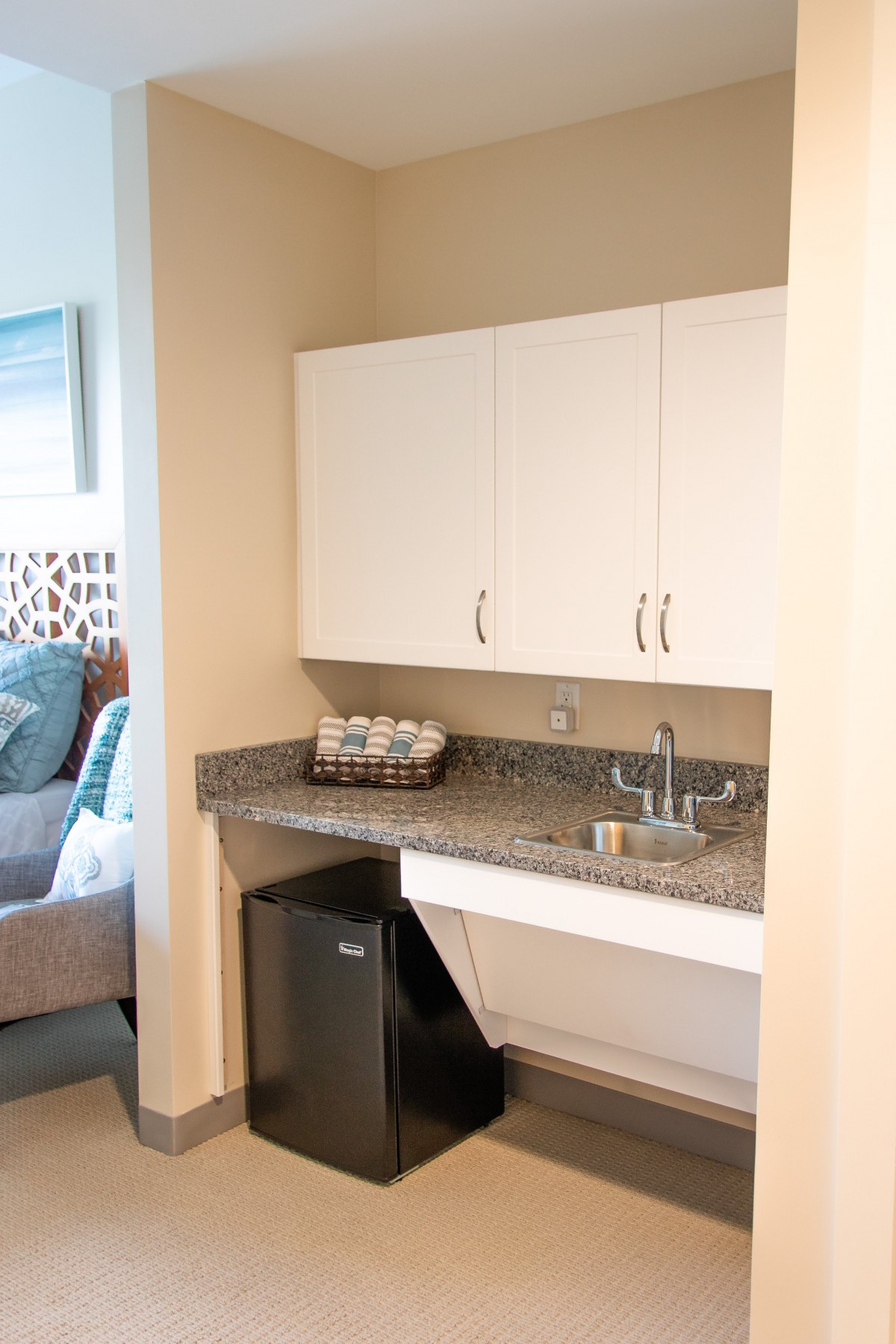 A compact kitchenette area with a mini fridge, sink, and storage cabinets.