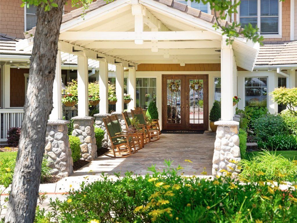 A charming front porch with rocking chairs and stone pillars, surrounded by lush landscaping.