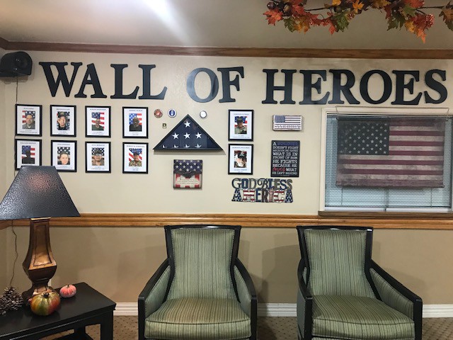 A wall decorated to honor heroes, featuring photographs, American flags, and seating.