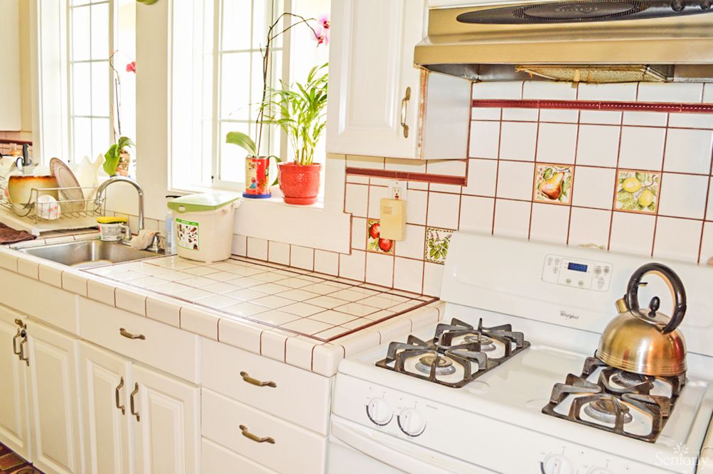 A bright kitchen with tiled surfaces, a stove, and potted plants by the window.