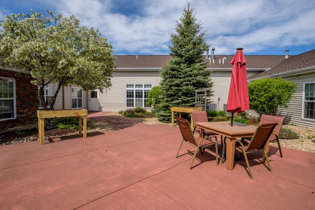 A backyard patio with outdoor furniture and a red umbrella, surrounded by trees.