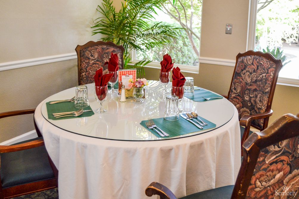 An elegantly set round dining table with red napkins and greenery in a cozy indoor restaurant.