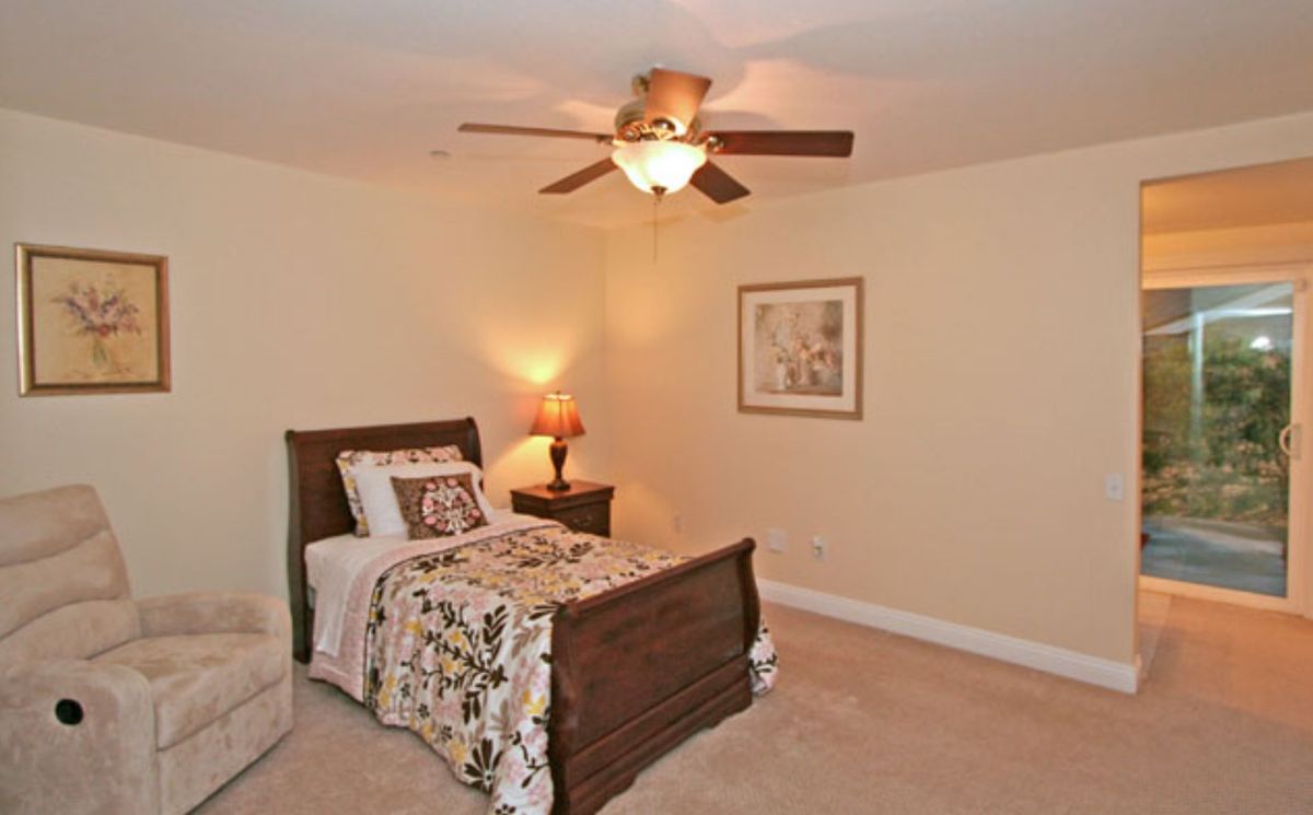 A cozy bedroom with a single bed, warm lighting, and a ceiling fan.