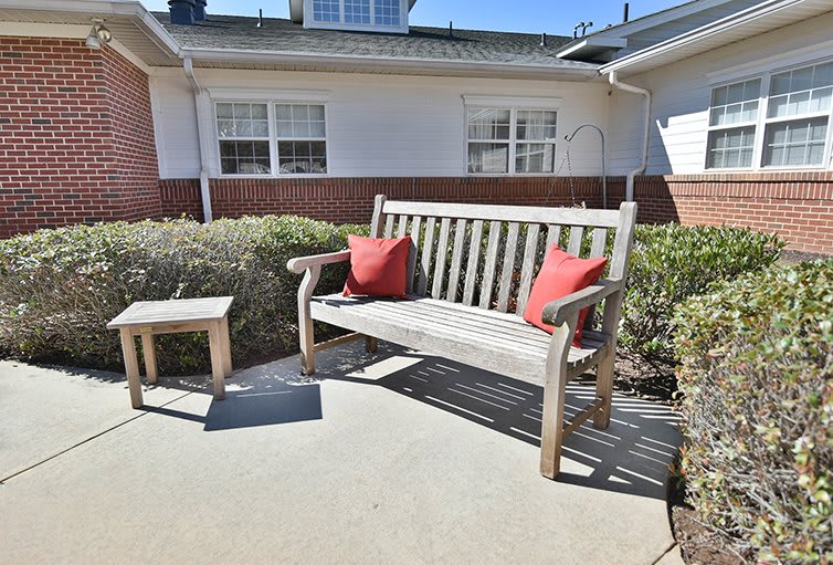 A wooden bench with red cushions on a sunny patio.