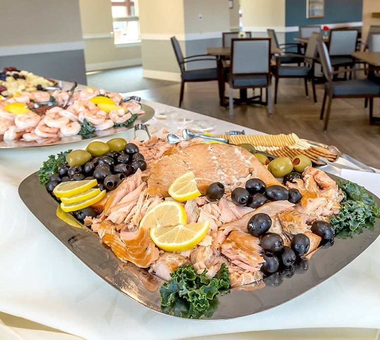A beautifully arranged buffet platter featuring slices of salmon garnished with lemons, olives, and greenery.