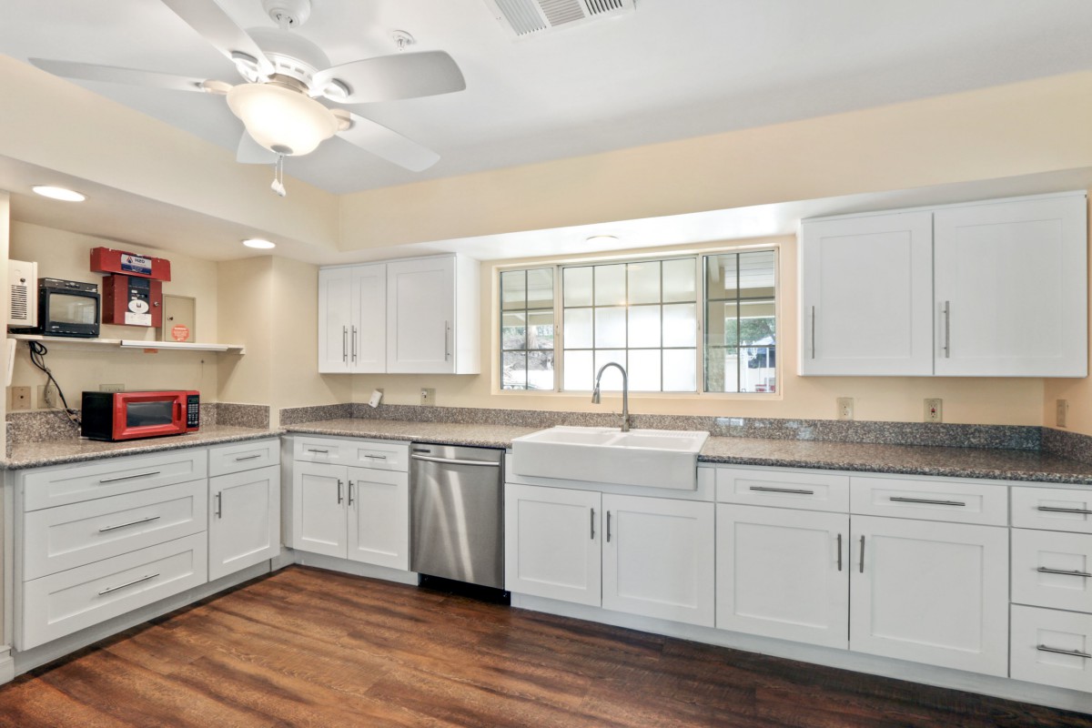 A modern kitchen featuring white cabinets, hardwood floors, and a farmhouse sink.