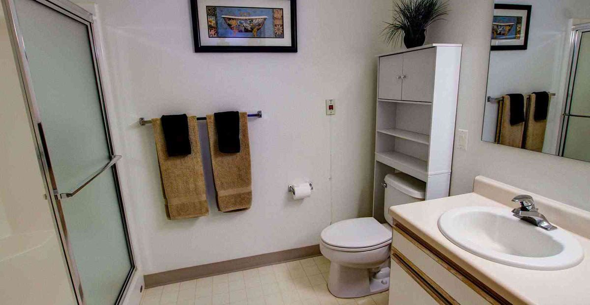 A neatly organized bathroom with a toilet, towel rack, storage shelf, and artwork on the wall.