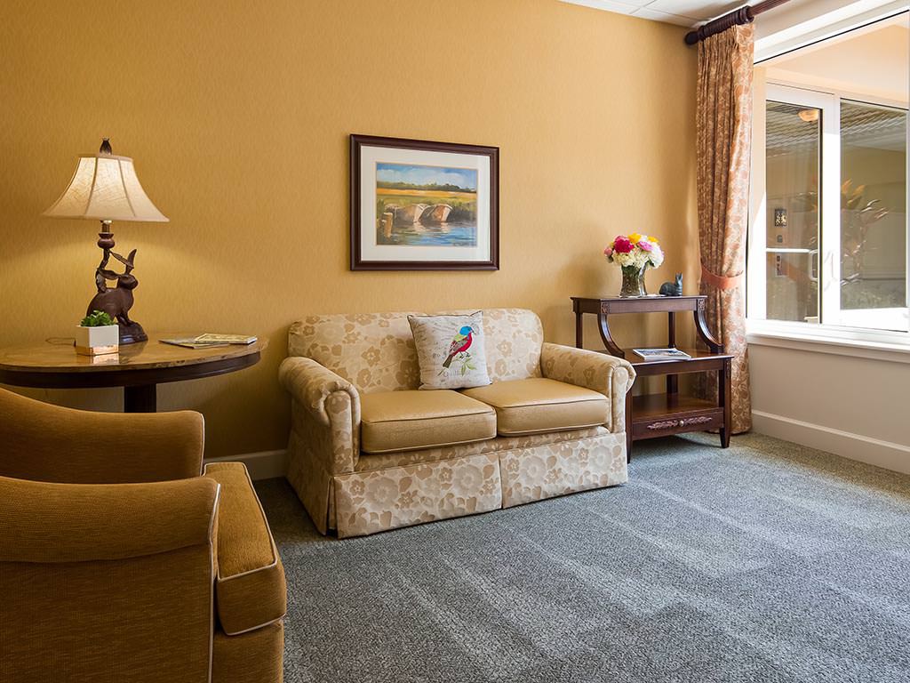 A cozy living room with a sofa, table, and lamp, featuring warm decor and a large window.
