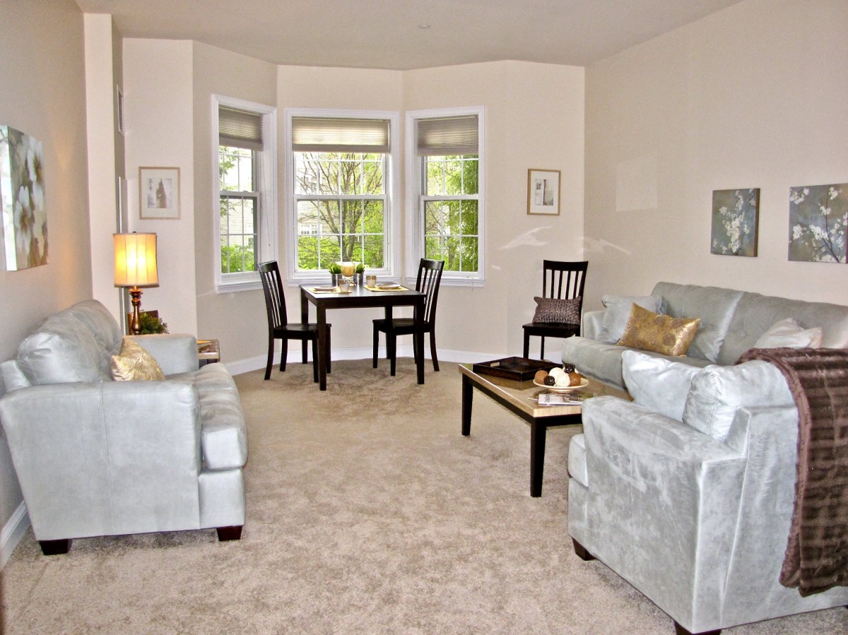 A cozy living room with a sofa set, coffee table, and a small dining area by the window.