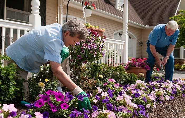 Two people tending to a flower garden in front of a house.