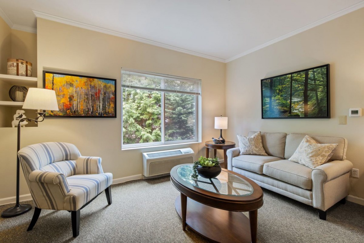 A cozy living room with a modern design, featuring a sofa, armchair, coffee table, and large window.